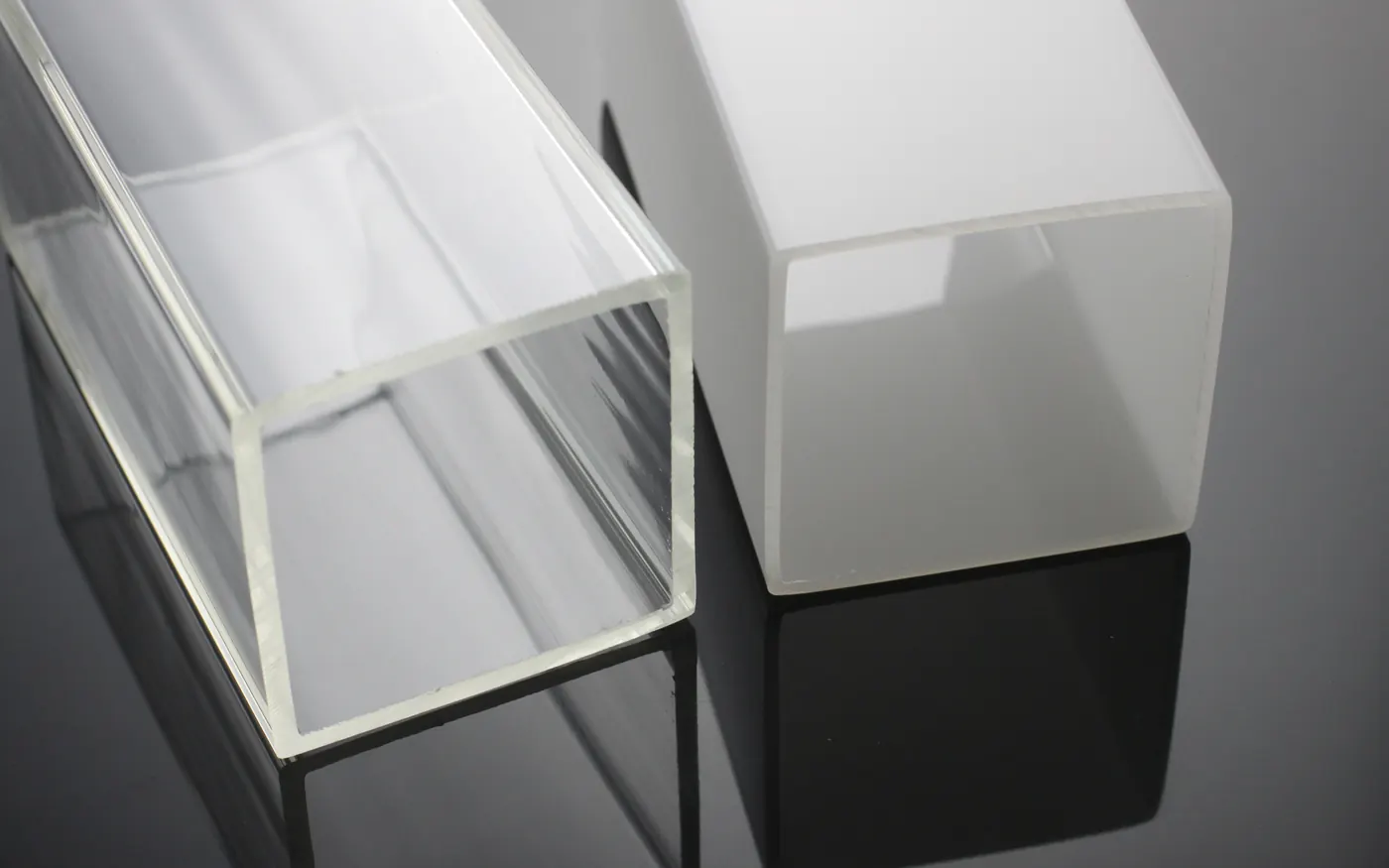 Clear and opal extruded acrylic square tubes standing on a dark surface